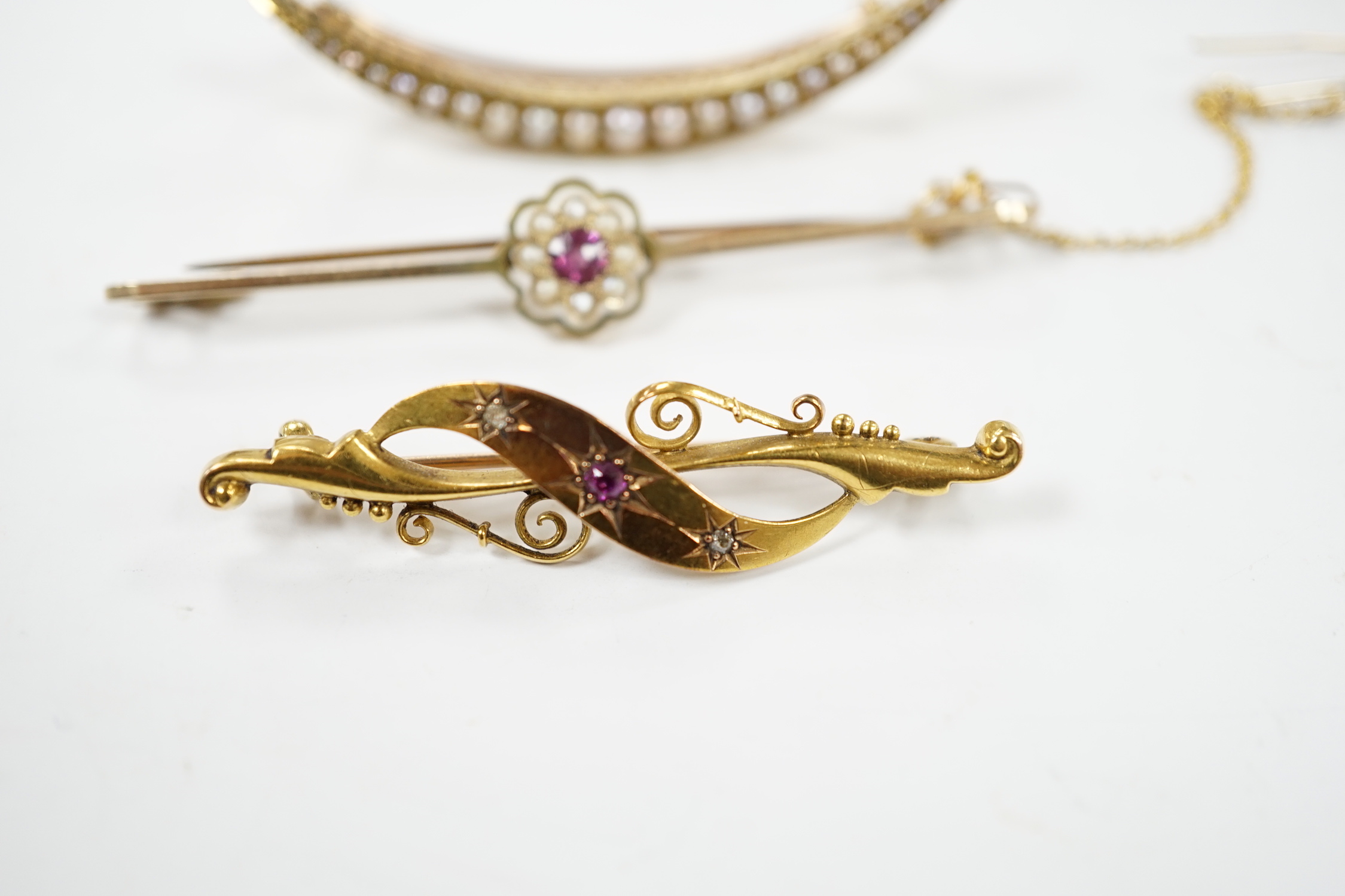 An Edwardian 15ct, ruby and diamond chip set three stone bar brooch, 45mm, a 9ct and gem set bar brooch and a yellow metal and seed pearl set crescent brooch.